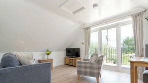 A modern living room with a grey sofa, a plaid armchair, a wooden coffee table, and a TV on a wooden cabinet. - 1 bedroom accommodation in Mickleton, near Chipping Campden (Mickleton, near Chipping Campden)