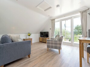 A modern living room with a grey sofa, a plaid armchair, a wooden coffee table, and a TV on a wooden cabinet. - 1 bedroom accommodation in Mickleton, near Chipping Campden (Mickleton, near Chipping Campden)