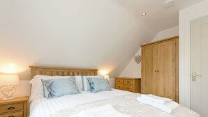 A bedroom with a wooden bed frame, white bedding, a nightstand with a lamp, a wooden dresser, and a wardrobe. - 1 bedroom accommodation in Mickleton, near Chipping Campden (Mickleton, near Chipping Campden)