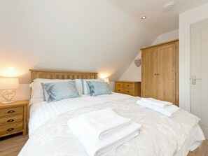 Une chambre à coucher avec un lit en bois, du linge de lit blanc, une table de chevet avec une lampe, une commode en bois et une armoire.