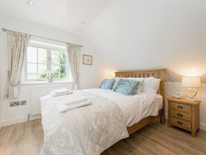 A bedroom with a bed, bedside table, lamp, and window with curtains. - 1 bedroom accommodation in Mickleton, near Chipping Campden (Mickleton, near Chipping Campden)