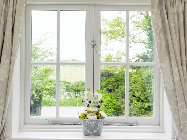 Une fenêtre donnant sur un paysage verdoyant, un cadre de fenêtre blanc et un vase de fleurs.