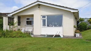 Een gelijkvloers huis met een groot raam, een klein terras met twee stoelen en een witte hek.
