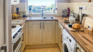 Een moderne keuken met houten kastjes, een roestvrijstalen spoelbak, een inbouwoven, een wasmachine en een raam met uitzicht op bomen.