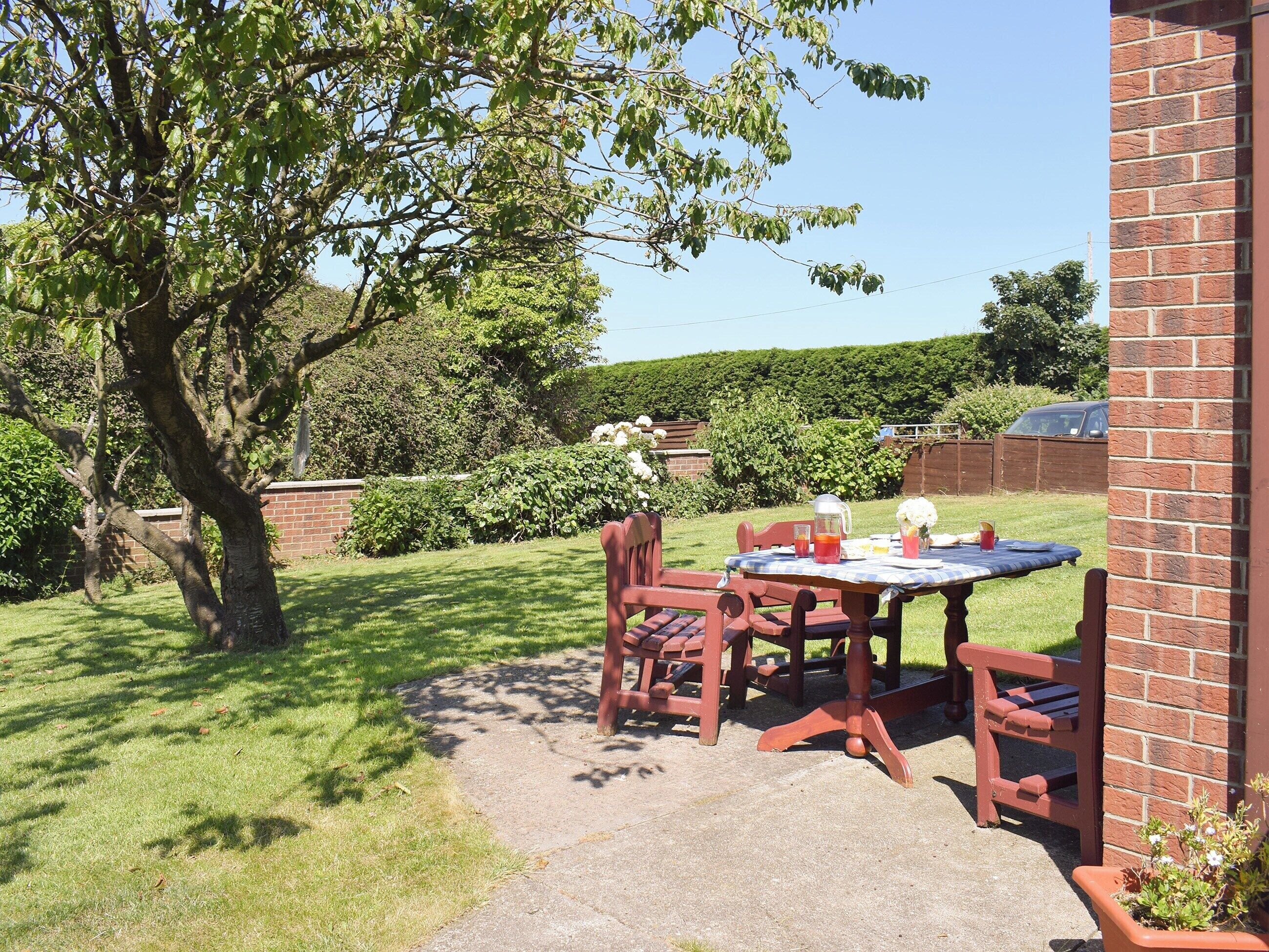 A patio with a table and chairs, surrounded by a brick wall and a hedge.