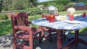 Une table de pique-nique recouverte d’une nappe à carreaux, entourée de chaises rouges. On y trouve des boissons, une carafe et une assiette remplie de nourriture.