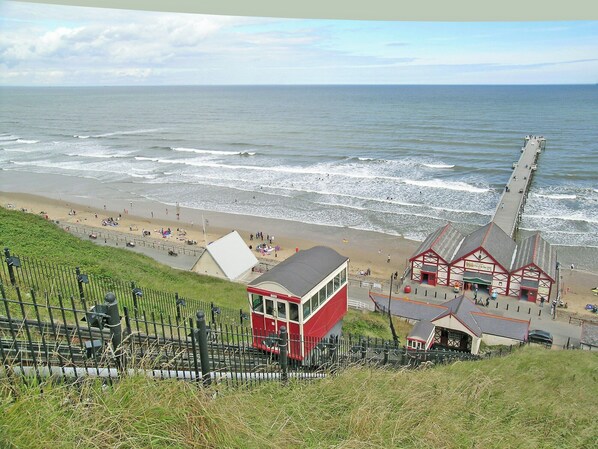 A coastal view with a beach, a pier, and a red building with a white roof.