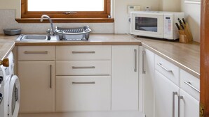 A kitchen with a sink, a dish rack, a microwave, and a washing machine. - Lochinchard Cottages (Kinlochbervie, Sutherland)