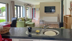 A modern kitchen with a built-in dishwasher, a dining area with a red chair, and a living room with a green sofa. - 1 bedroom accommodation in Moorlinch, near Bridgwater (Moorlinch, near Bridgwater)
