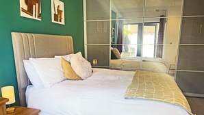 A neatly made bed with white and yellow bedding, a wooden nightstand with a lamp, and a red chair. - 1 bedroom accommodation in Moorlinch, near Bridgwater (Moorlinch, near Bridgwater)