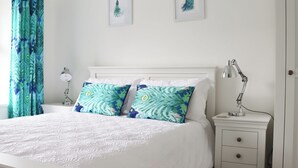 Ein Schlafzimmer mit einem weißen Bett, zwei Kissen mit Blattmuster, einem Nachttisch mit Lampe und einer Tür.