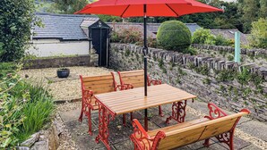 Eine Terrasse mit Tisch und Bänken, einem roten Sonnenschirm und einer Steinmauer.