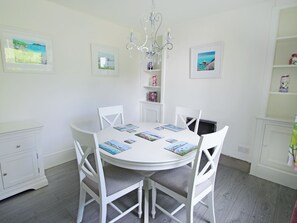 Uma sala de jantar clara com uma mesa redonda, quatro cadeiras, um lustre e quadros nas paredes.