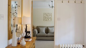 A hallway with a wooden dresser, a mirror, and a radiator. There is a sofa and a wall with a decorative piece in the background.