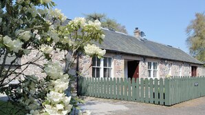 A stone house with a gravel driveway and a wooden fence.