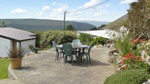 Une terrasse avec une table et des chaises, entourée de plantes et de fleurs en pot.