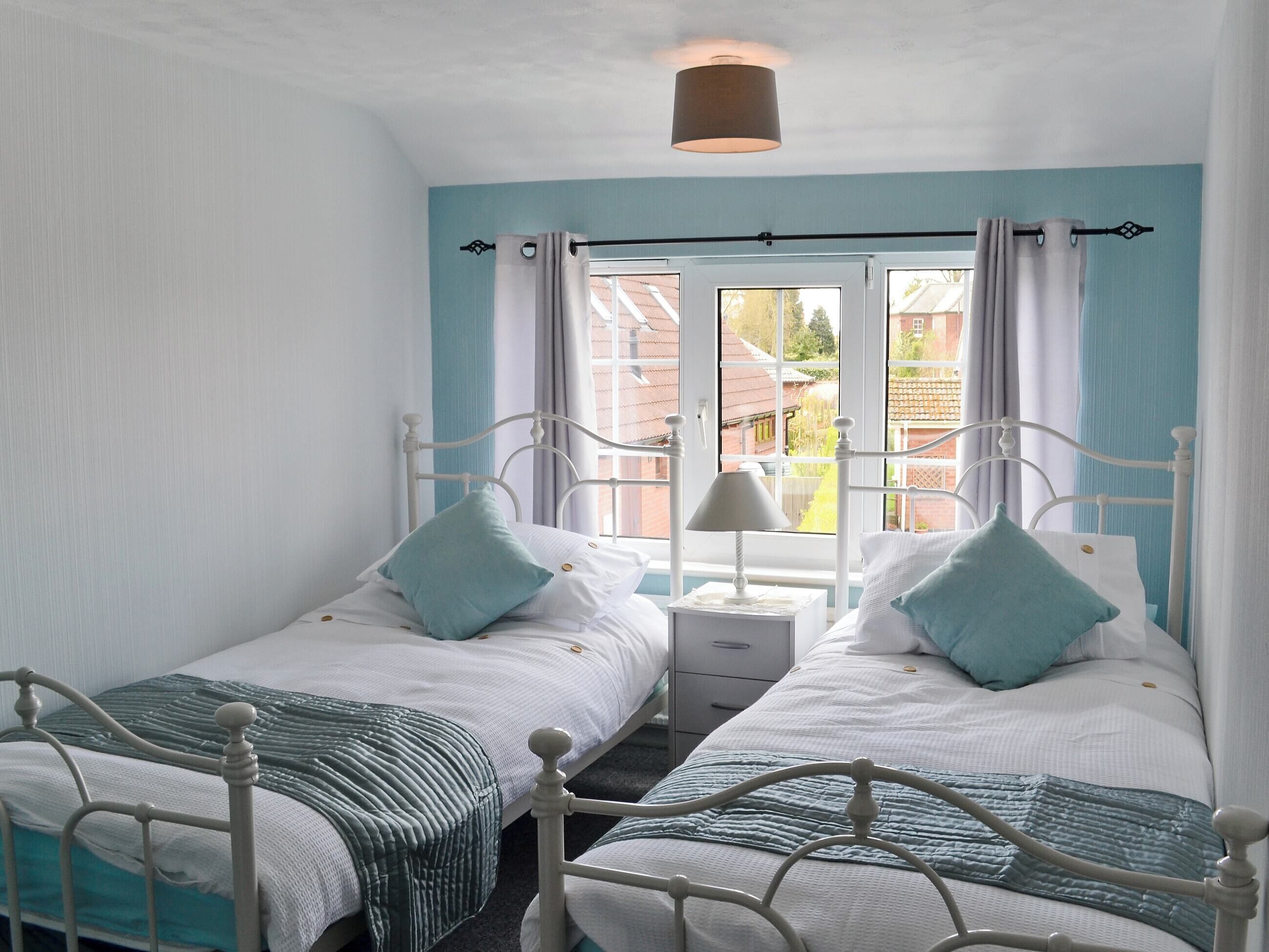 A twin bedroom with two beds, a nightstand, a lamp, and a window with curtains.