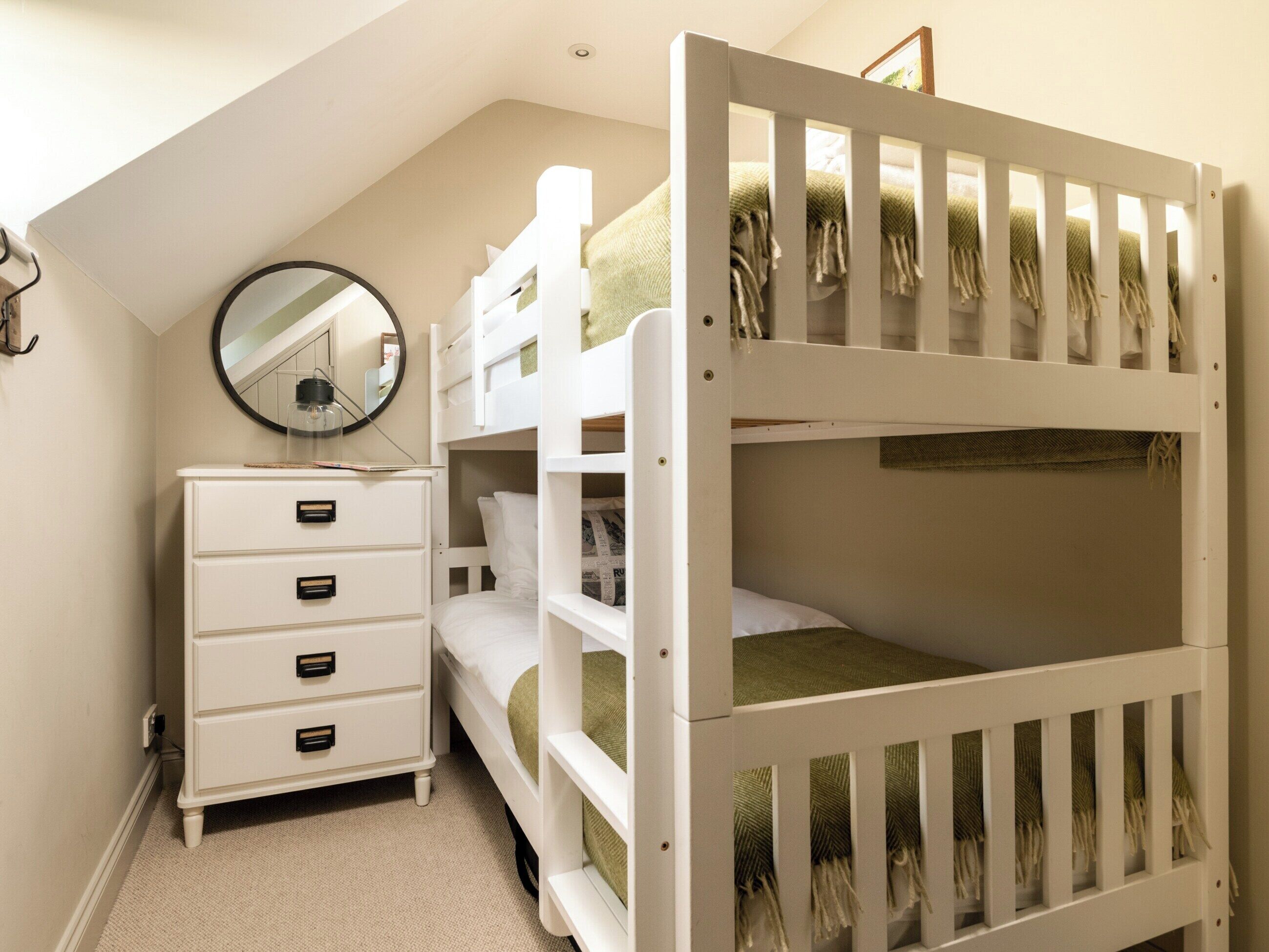 Een slaapkamer met een stapelbed, een dressoir met lades, een ronde spiegel en een plafondlamp.