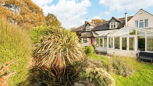 Una casa con un invernadero, un estanque y abundante vegetación alrededor.