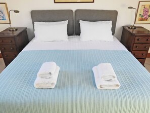 Uma cama de casal com um cobre-leito azul listrado, duas almofadas brancas e duas toalhas brancas dobradas na cama.