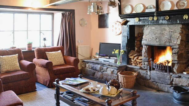 A cozy living room with a fireplace, comfortable seating, and a television. - Birkerthwaite Farmhouse (Eskdale)