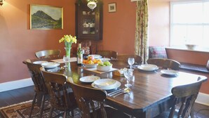 A dining room with a wooden table set for six, surrounded by chairs. A floral vase and a bottle of wine are on the table. - Birkerthwaite Farmhouse (Eskdale)