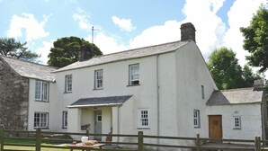 A two-story white building with a stone extension, a wooden fence, and a picnic table with a basket and a jug. - Birkerthwaite Farmhouse (Eskdale)
