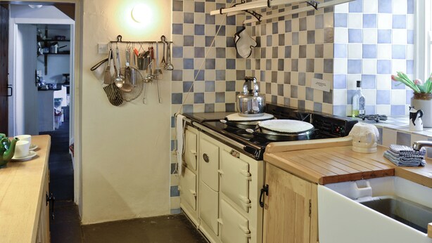Una cocina con salpicadero a cuadros, una estufa y varios utensilios de cocina colgados en la pared.