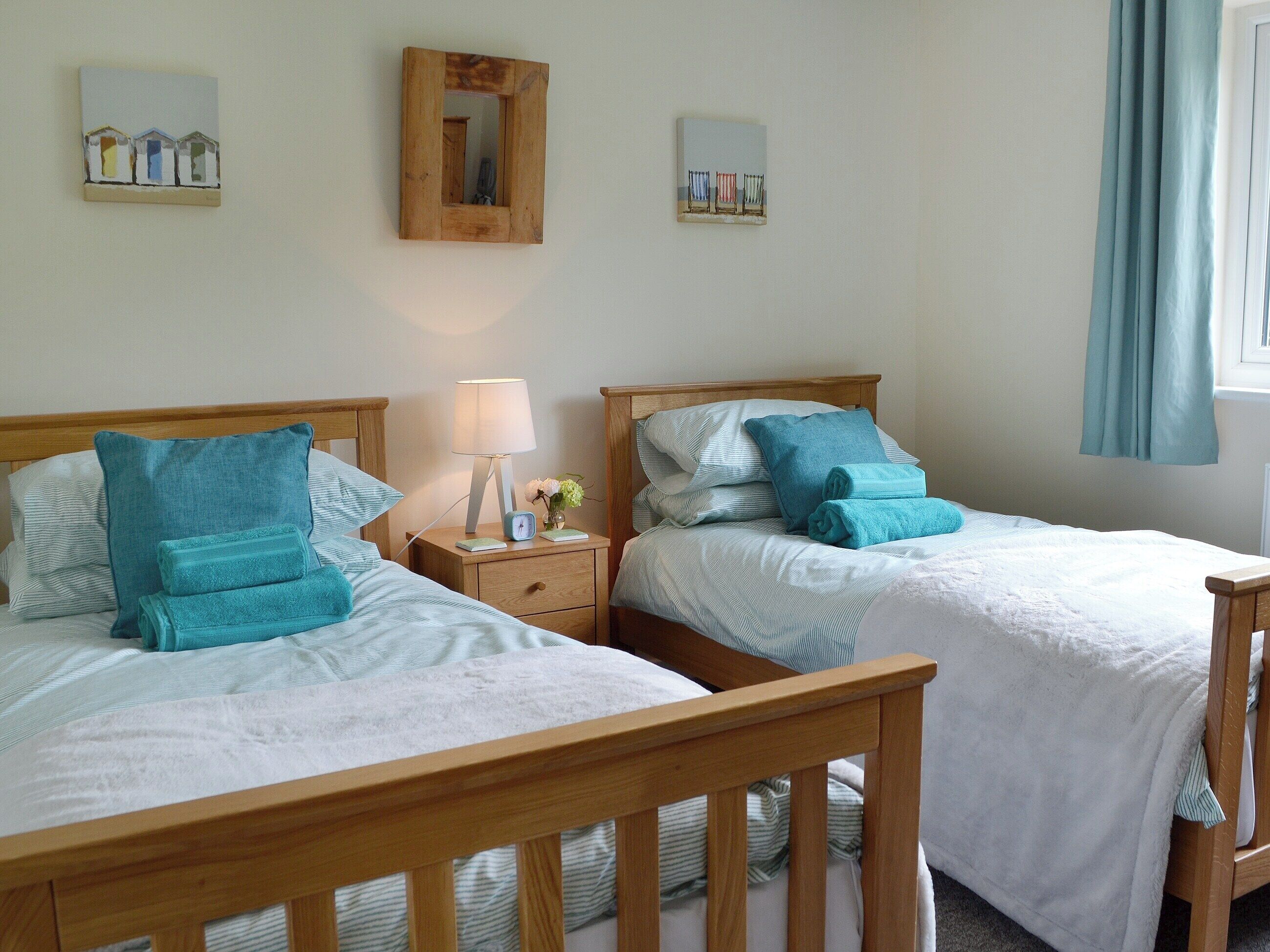 Two twin beds with wooden headboards, white bedding, and teal pillows.