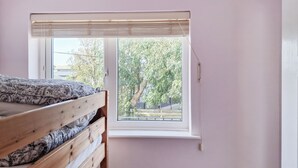 A bedroom with a single bed, a window with blinds, and a view of trees outside. - Brightlands Apartment (Bude)