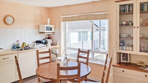 A kitchen with a round wooden table, white cabinets, and a window with a view of the outside. - Brightlands Apartment (Bude)