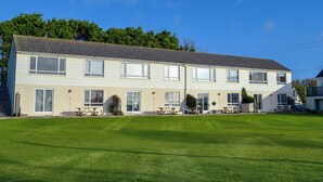 A two-story building with a flat roof, multiple windows, and a grassy lawn in front. - Brightlands Apartment (Bude)