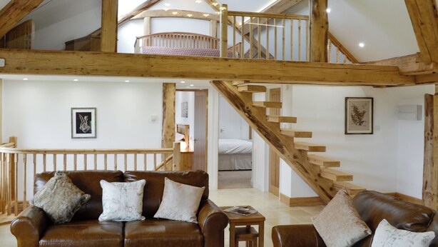 A spacious loft with exposed wooden beams, a wooden staircase, a leather sofa, and a small table.