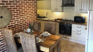 Een keuken met witte kasten, een bakstenen muur en een eethoek met geweven stoelen en een houten tafel.