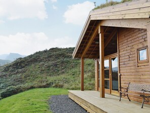 Een houten chalet met terras, grote ramen en een bankje.