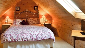 A cozy attic bedroom with a sloped ceiling, a wooden headboard, two bedside lamps, and a bed with patterned bedding. - 3 bedroom accommodation in Laytham, near York (Laytham, near York)