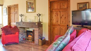 A cozy living room with a fireplace, a red armchair, a television, and wooden doors. - 3 bedroom accommodation in Laytham, near York (Laytham, near York)