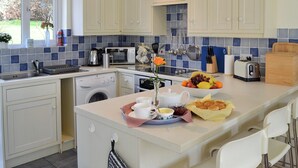 Una cocina moderna con armarios blancos, microondas integrado y un lavabo. Hay un frutero en la encimera y una tostadora.