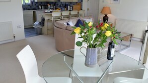 Una cocina moderna con armarios blancos, un comedor con mesa de vidrio y un jarrón con flores.