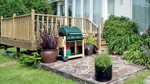 Un patio con una parrilla, plantas en macetas y una terraza de madera.