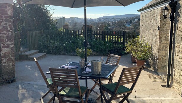 En terrasse med et bord, stole og en parasol, med udsigt til en by i baggrunden.