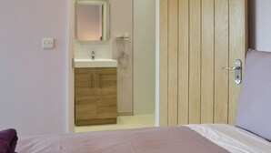 A bedroom with a bed, a wooden wardrobe, a bathroom with a sink and mirror, and a door leading to another room. - Lucy's Lodge - UKC2202 (Doddington, near Lincoln)