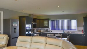 A modern kitchen with built-in appliances, a dining area with chairs, and a leather sofa. - Lucy's Lodge - UKC2202 (Doddington, near Lincoln)