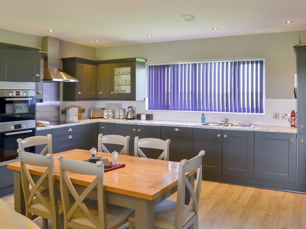 A modern kitchen with dark cabinets, a wooden dining table, and a window with blinds.