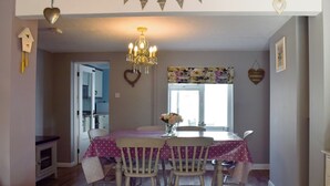 A dining area with a chandelier, heart-shaped decorations, and a floral window valance. - 2 bedroom accommodation in Pakefield, near Lowestoft (Pakefield, near Lowestoft)