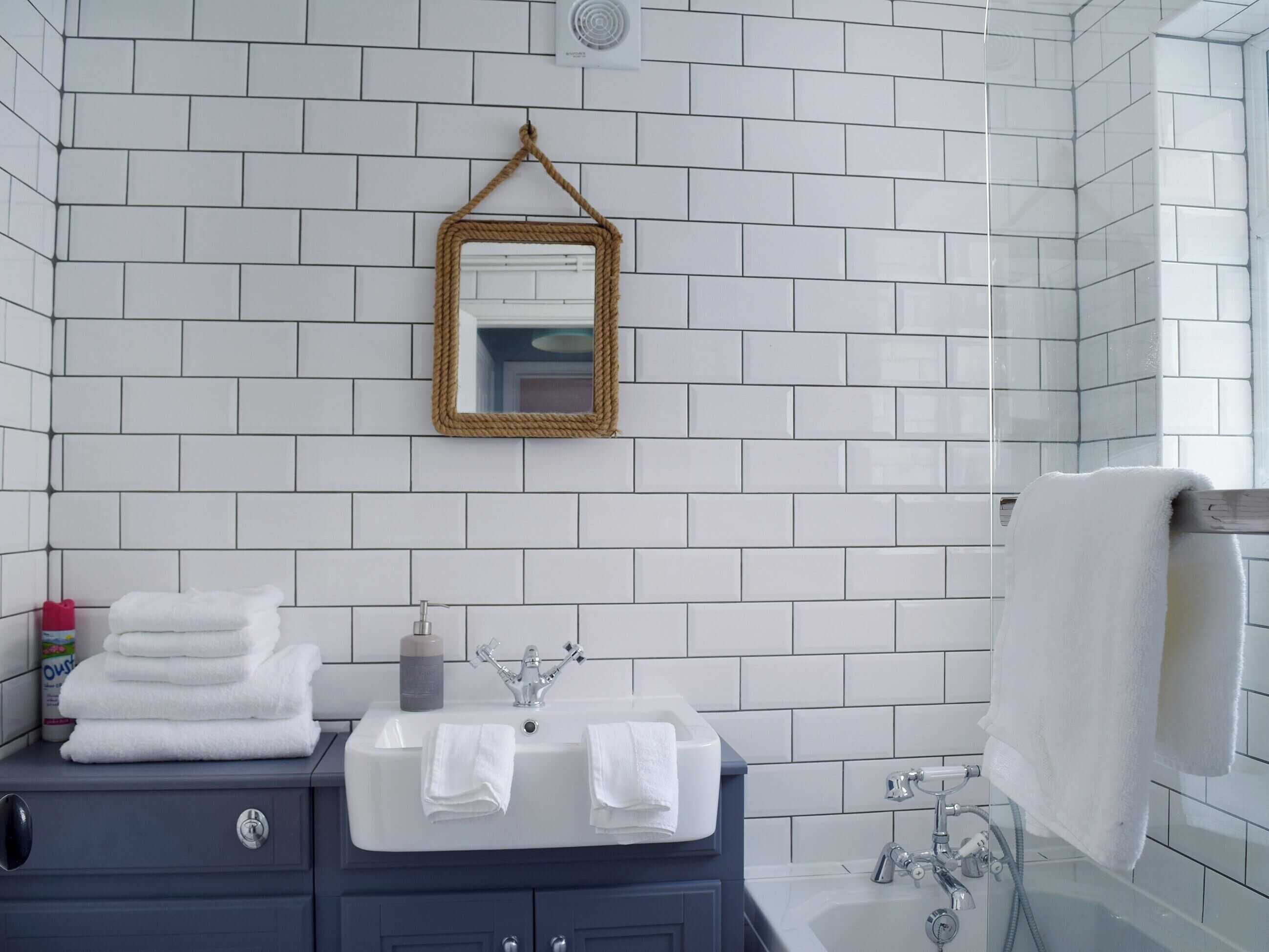 A bathroom with white tiled walls, a blue vanity with a sink, two towels, a mirror with a gold frame, and a shower area.