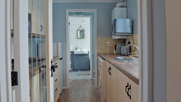 A narrow kitchen with a sink, a microwave, and a hanging light fixture. - 2 bedroom accommodation in Pakefield, near Lowestoft (Pakefield, near Lowestoft)