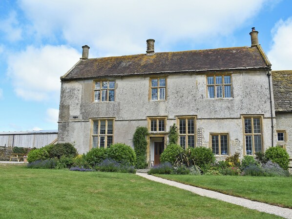 A two-story stone building with multiple windows, a front door, and a gravel pathway leading to the entrance.