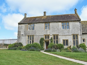 A two-story stone building with multiple windows, a front door, and a gravel pathway leading to the entrance.