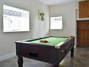 A pool table with balls, a painting, and windows with curtains.